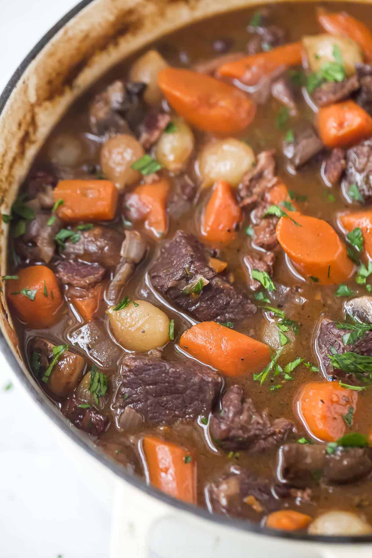 a pot of beef bourguignon with carrots, pearl onions, and mushrooms in a dark gravy