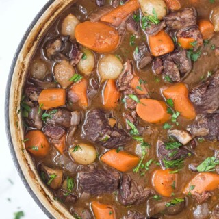 a pot of beef bourguignon with carrots, pearl onions, and mushrooms in a dark gravy
