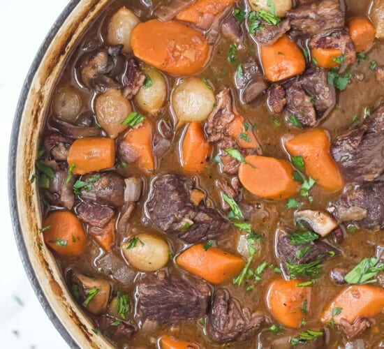 a pot of beef bourguignon with carrots, pearl onions, and mushrooms in a dark gravy