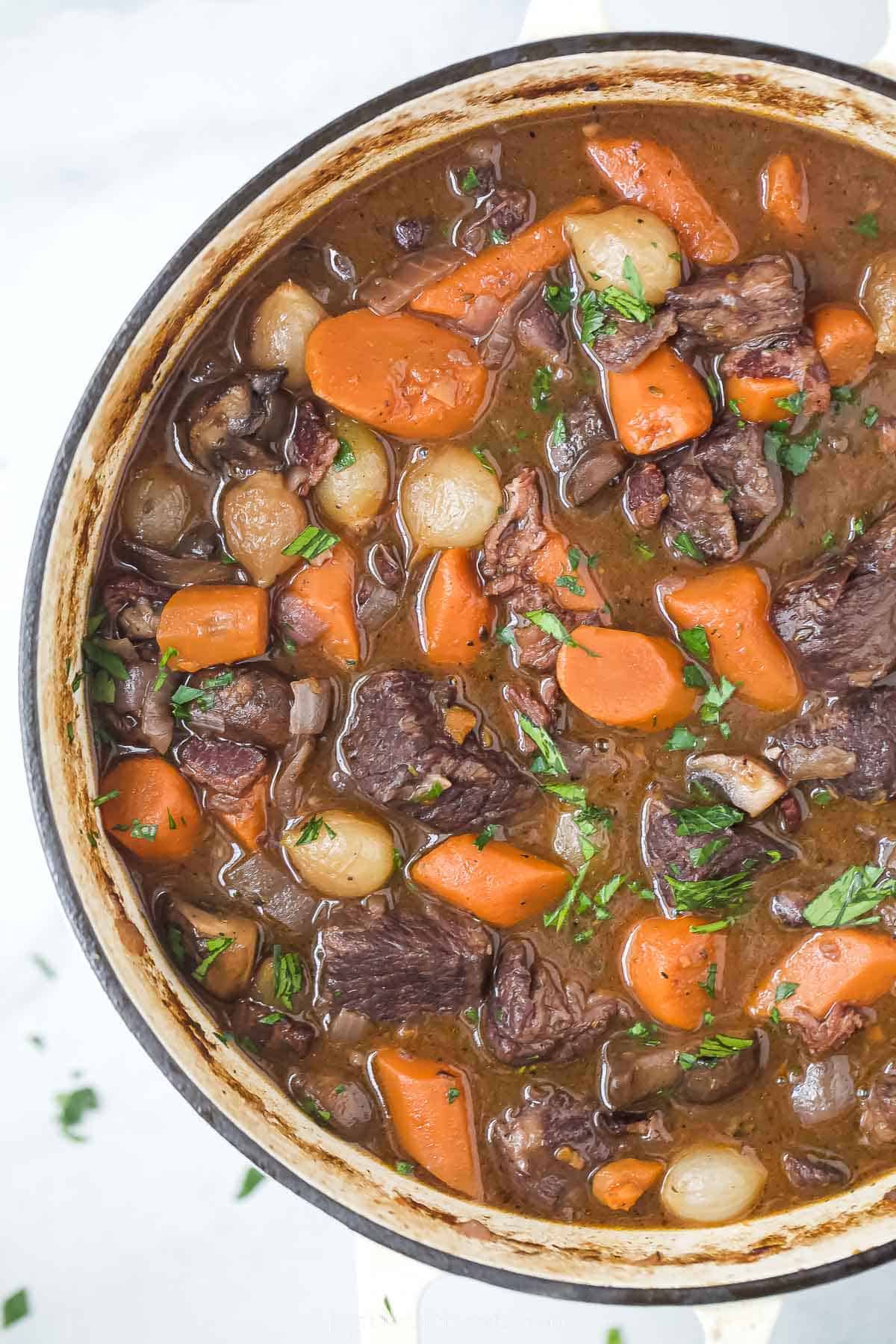 a pot of beef bourguignon with carrots, pearl onions, and mushrooms in a dark gravy