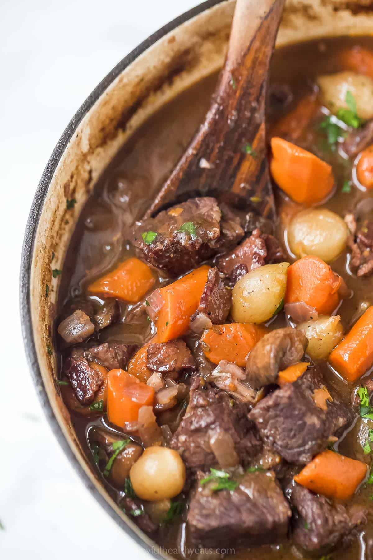 a pot of beef bourguignon with carrots, pearl onions, and mushrooms in a dark gravy