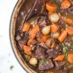 a pot of beef bourguignon with carrots, pearl onions, and mushrooms in a dark gravy