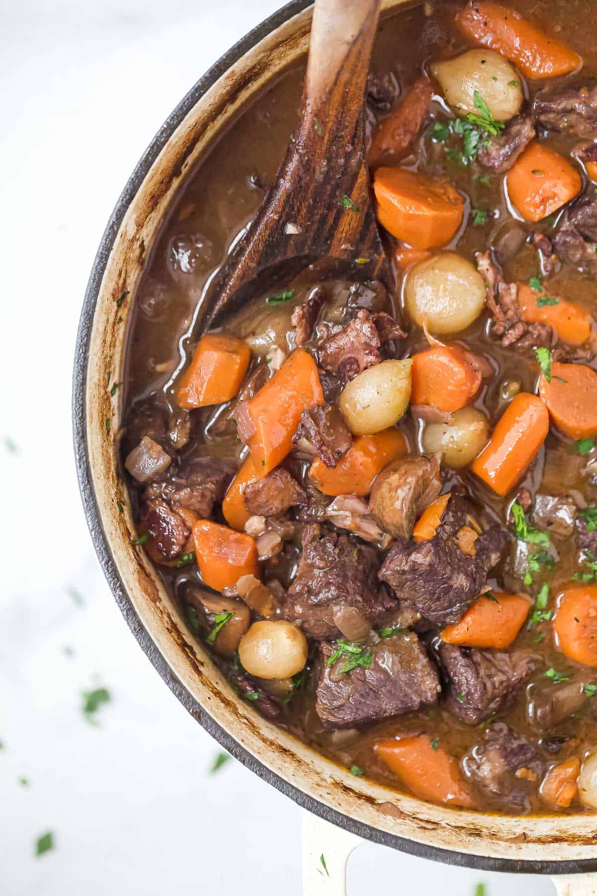 a pot of beef bourguignon with carrots, pearl onions, and mushrooms in a dark gravy