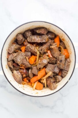 chunks of cooked beef in a dutch oven with carrots and onions