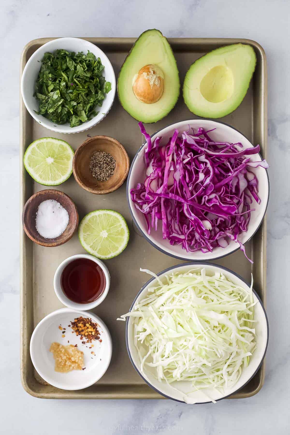 ingredients to make creamy coleslaw for fish tacos includig shredded cabbage, limes, avocado, cilantro, and seasonings