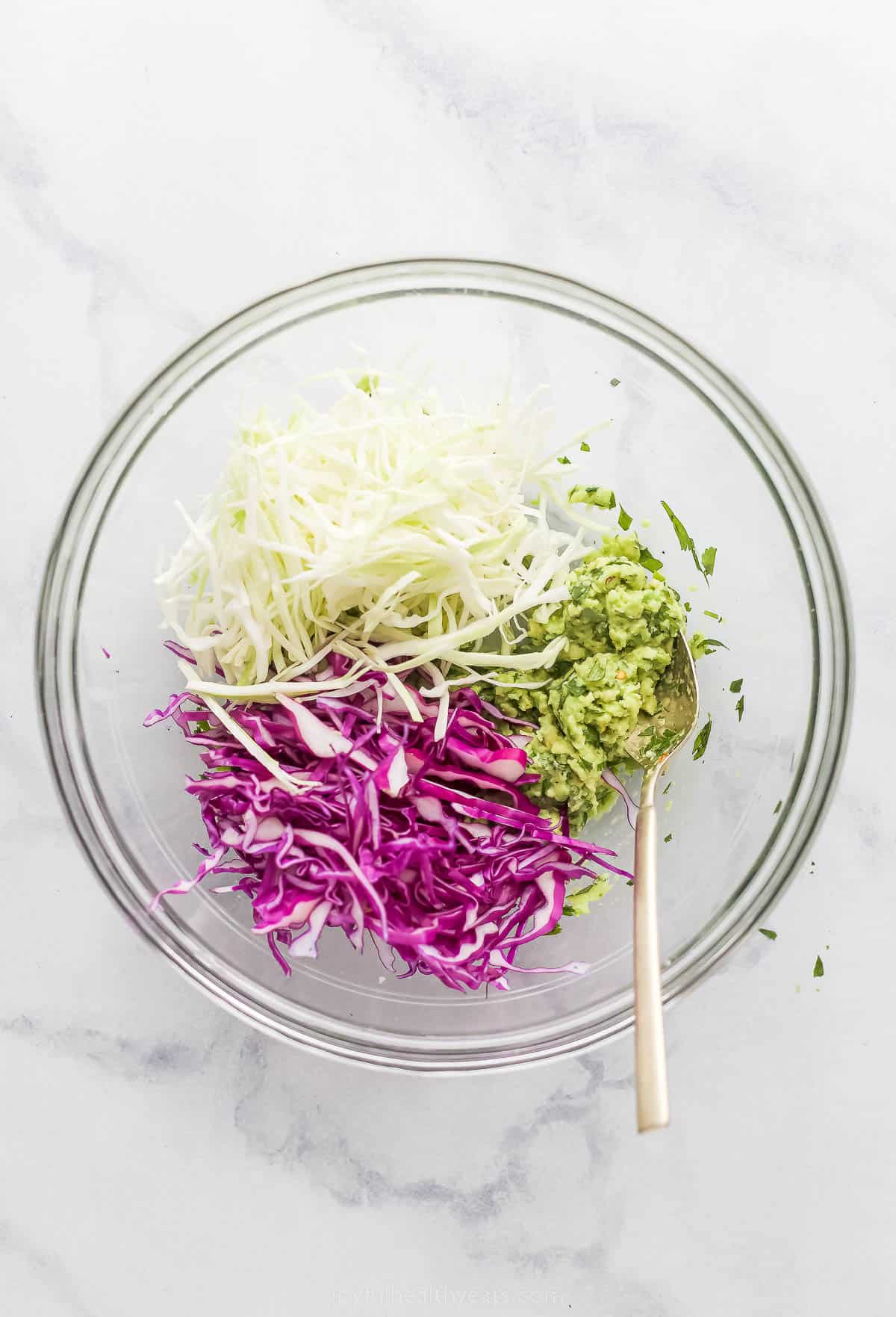 This Creamy Coleslaw for Fish Tacos is made with avocado instead of mayo. The smooth avocado-based dressing has cilantro, garlic, and lime. shredded cabbage and mashed avocado in a bowl