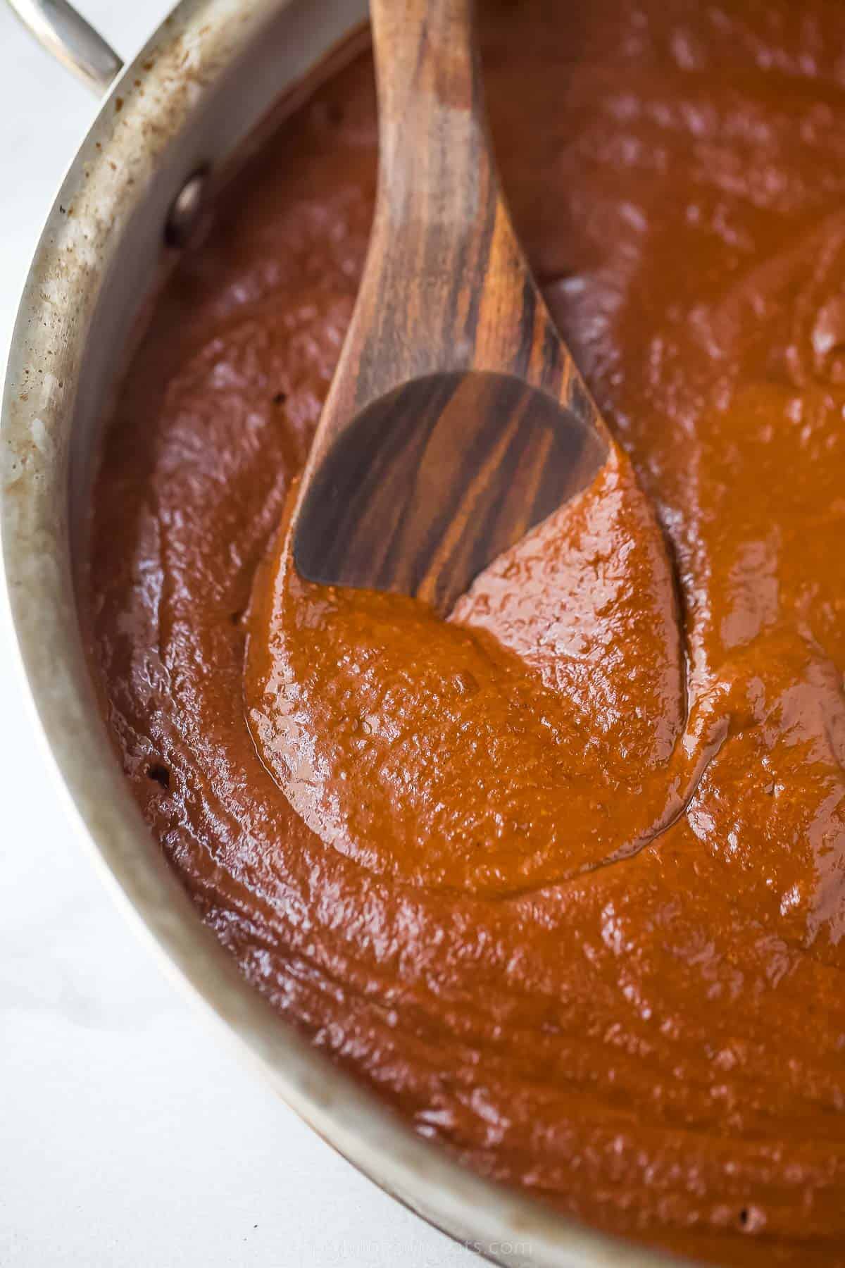a dark brown and red sauce in a large pot with a wooden spoon