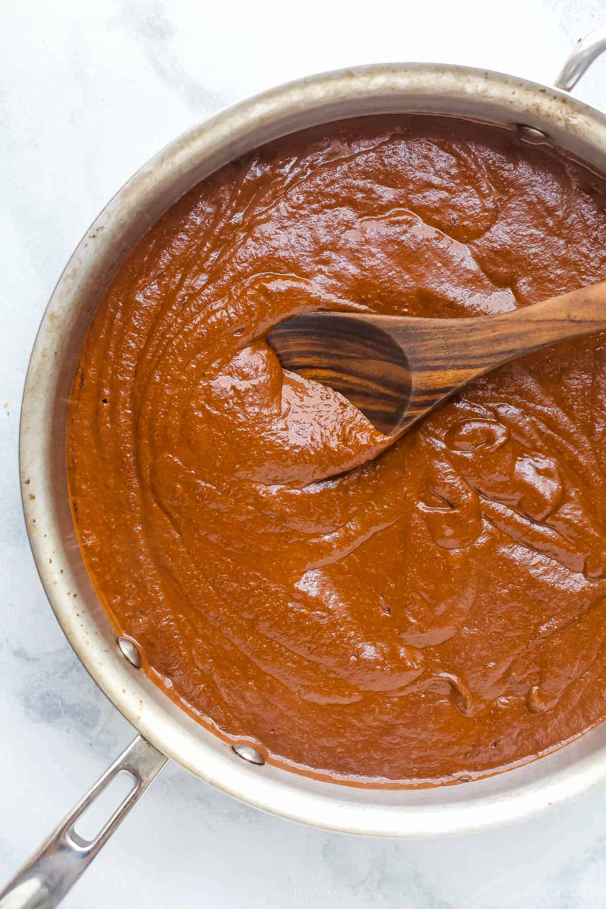 a dark brown and red sauce in a large pot with a wooden spoon