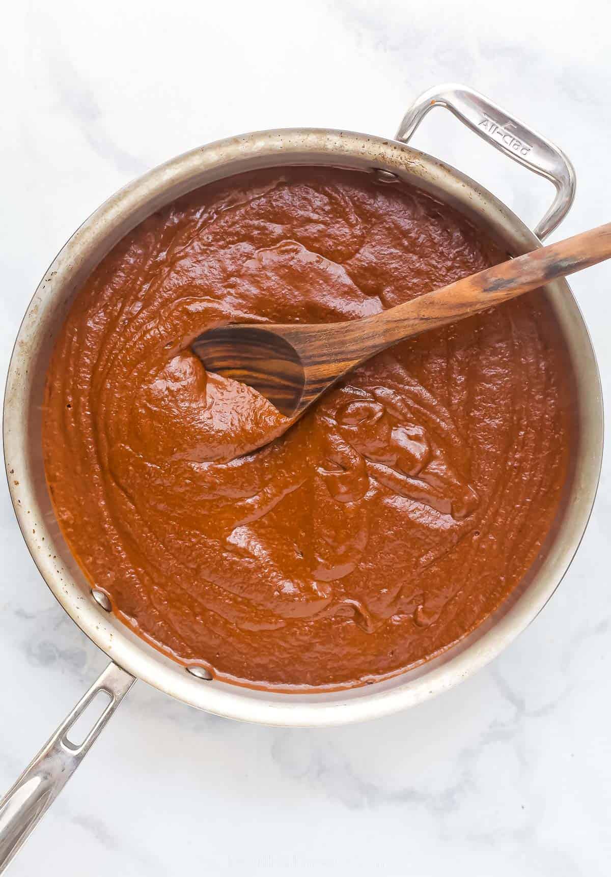 a dark brown and red sauce in a large pot with a wooden spoon