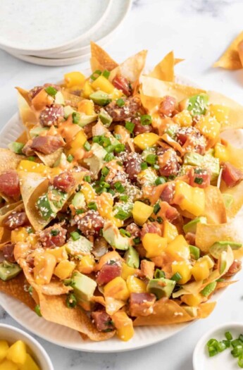 a plate of ahi tuna poke nachos with diced mango, green onions, and sriracha mayo
