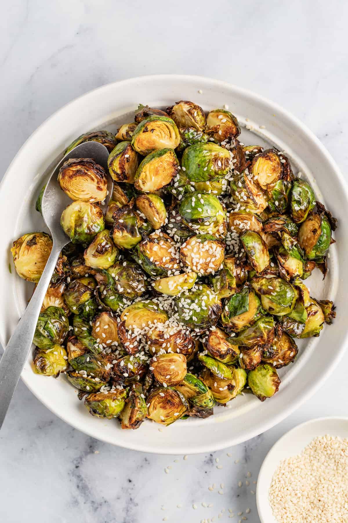 These Crispy Asian Air Fryer Brussels Sprouts are crunchy little bites filled with lots of soy, ginger, garlic, and spicy flavor. a bowl of crispy brussels sprouts with a spoon
