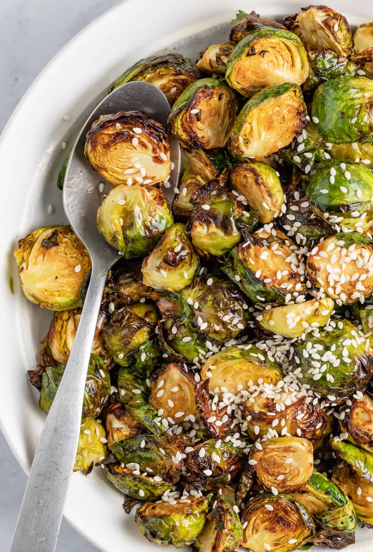 These Crispy Asian Air Fryer Brussels Sprouts are crunchy little bites filled with lots of soy, ginger, garlic, and spicy flavor. a bowl of asian-inspired brussels sprouts with sesame seed garnish