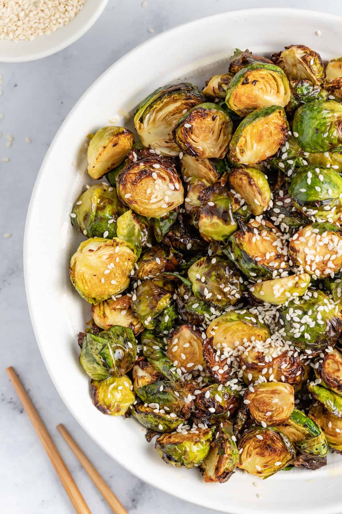 These Crispy Asian Air Fryer Brussels Sprouts are crunchy little bites filled with lots of soy, ginger, garlic, and spicy flavor. a bowl of asian-inspired brussels sprouts with sesame seed garnish