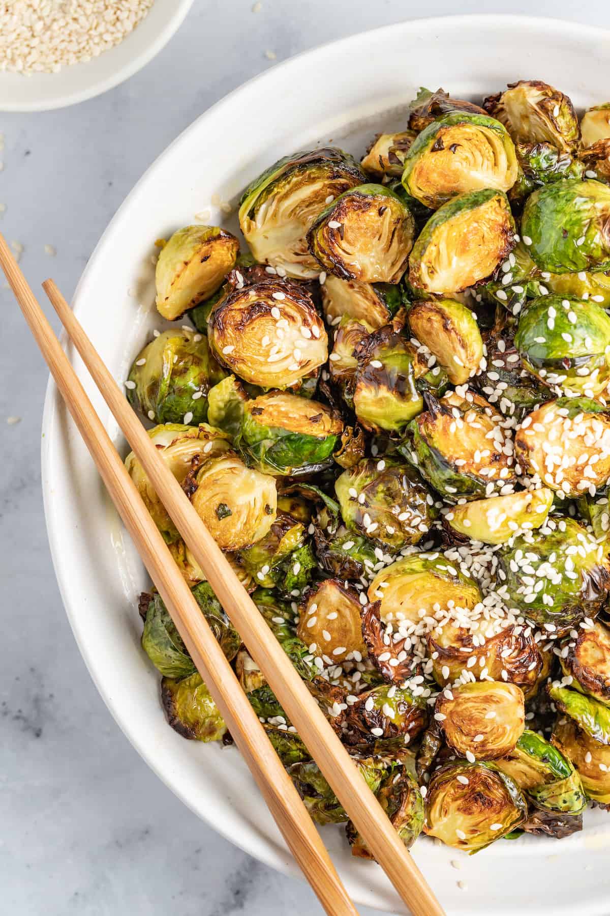 These Crispy Asian Air Fryer Brussels Sprouts are crunchy little bites filled with lots of soy, ginger, garlic, and spicy flavor. a bowl of crispy fried brussels sprouts and chopsticks