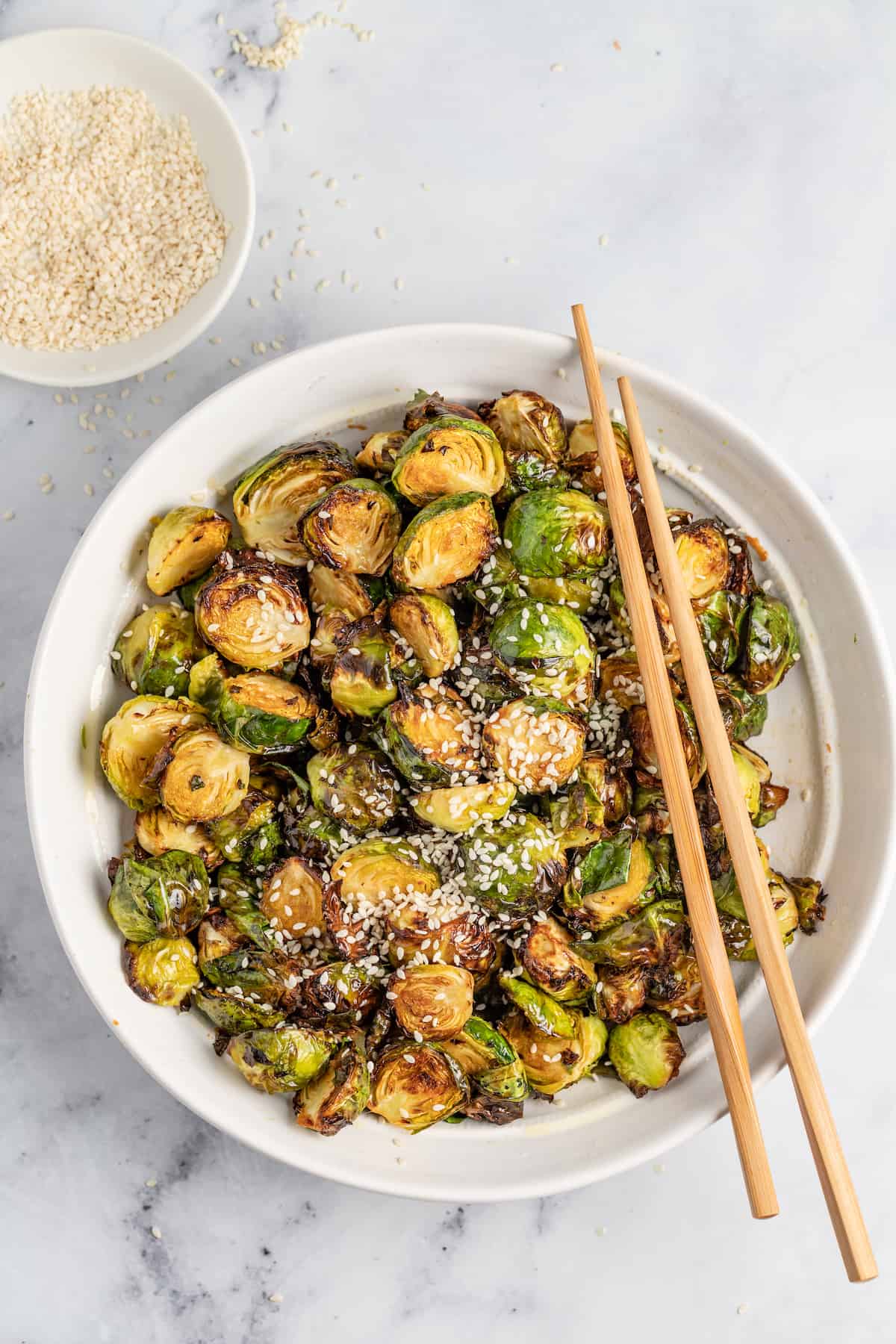 These Crispy Asian Air Fryer Brussels Sprouts are crunchy little bites filled with lots of soy, ginger, garlic, and spicy flavor. a bowl of crispy fried brussels sprouts and chopsticks
