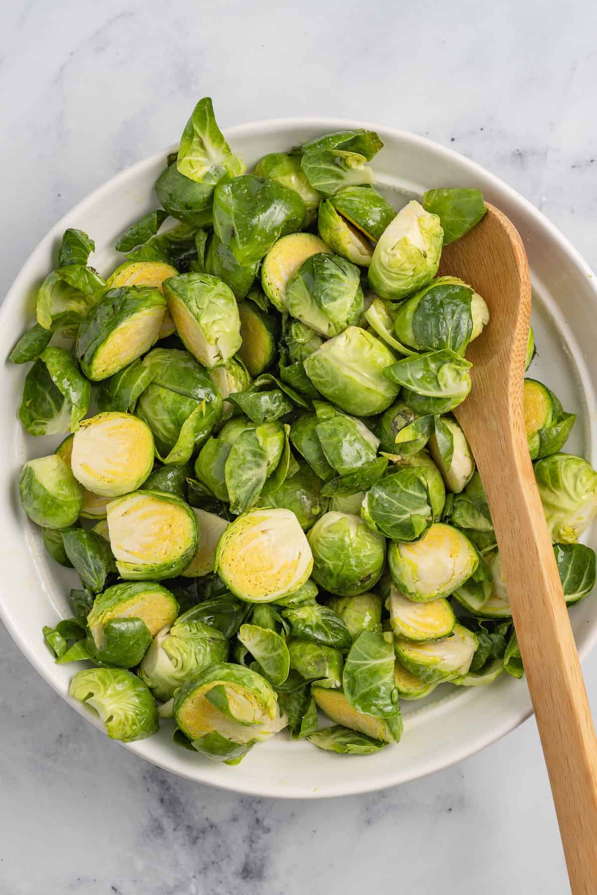 a bowl of brussels sprouts getting tossed with a wooden spoon