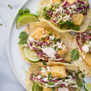 a plate of tacos with fried fish, slaw, and crema