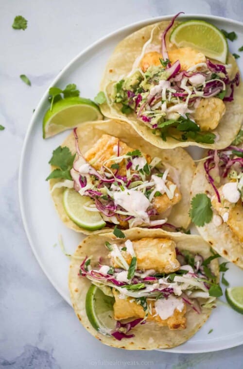 a plate of tacos with fried fish, slaw, and crema