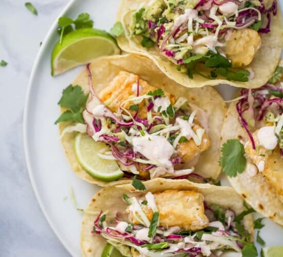 a plate of tacos with fried fish, slaw, and crema