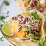 a fish taco on a plate with lime garnish and slaw on top