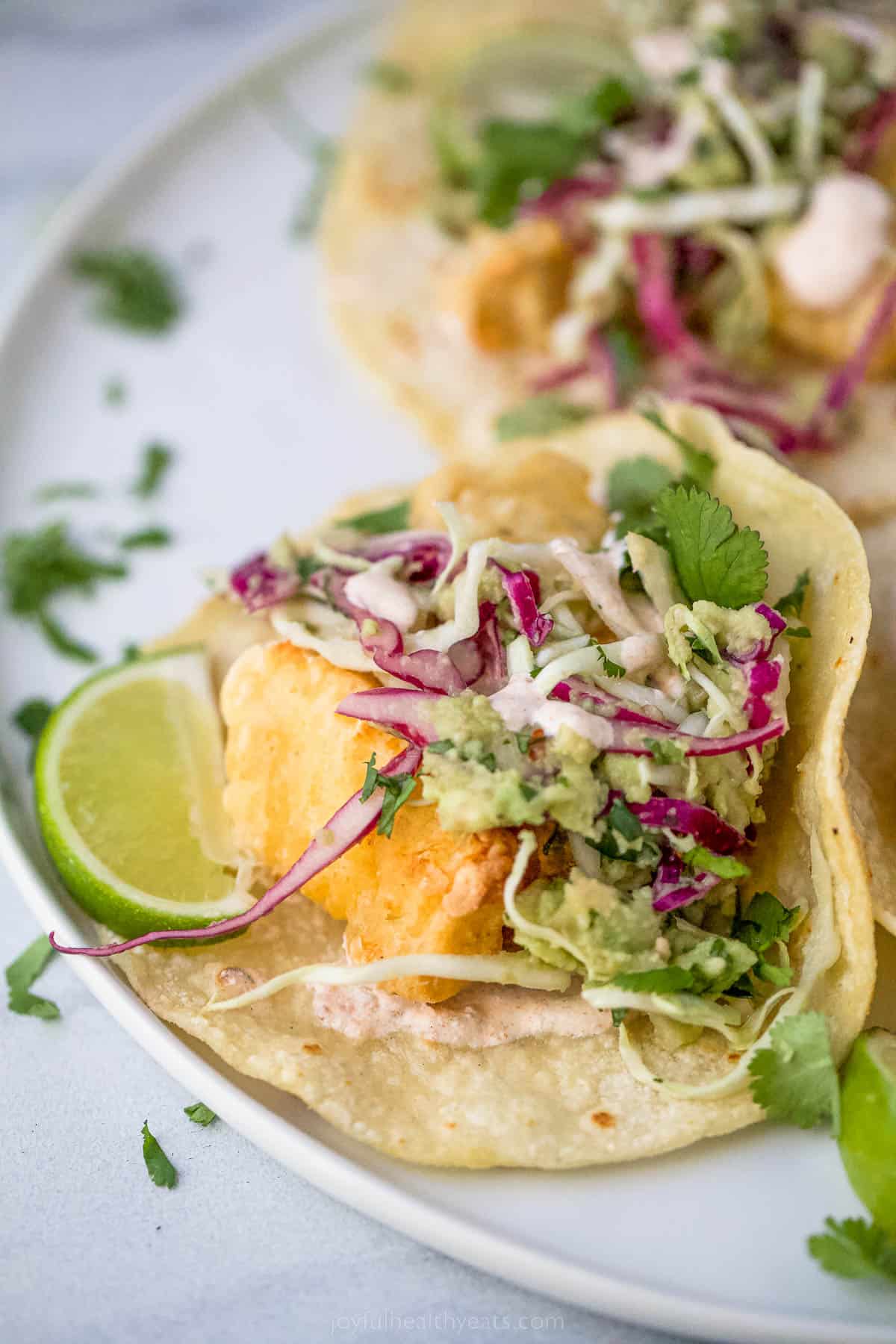 a fish taco on a plate with lime garnish and slaw on top