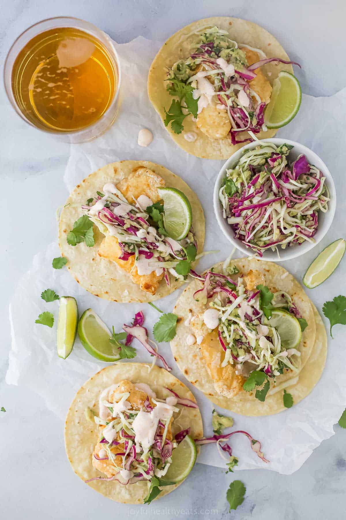 Beer Battered Air Fryer Fish Tacos are dipped in a tasty batter and fried the healthy way! Add slaw and Chipotle Crema for the perfect taco! top view of air fryer beer battered fish tacos with slaw and lime wedge as a garnish
