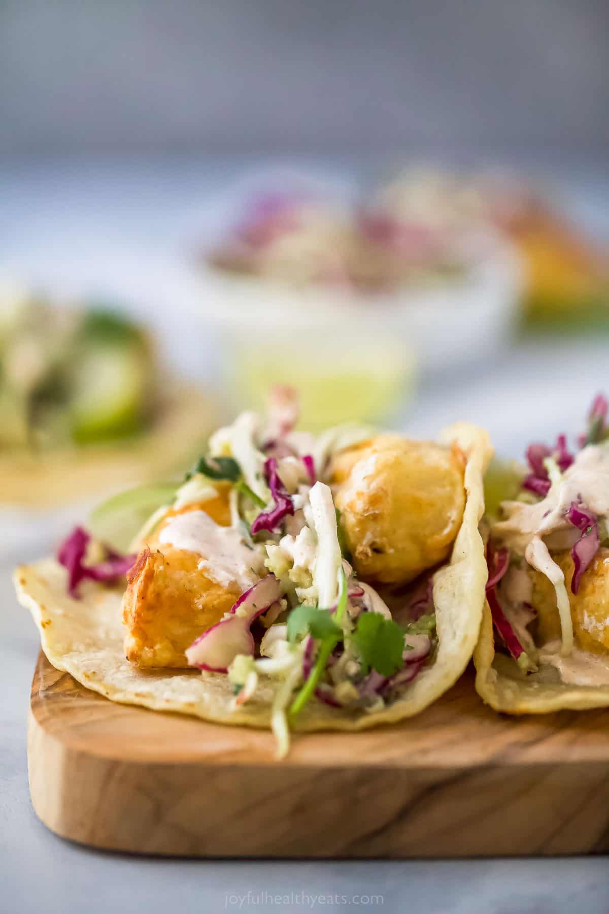 side view of a taco with fried fish, coleslaw, and crema topping