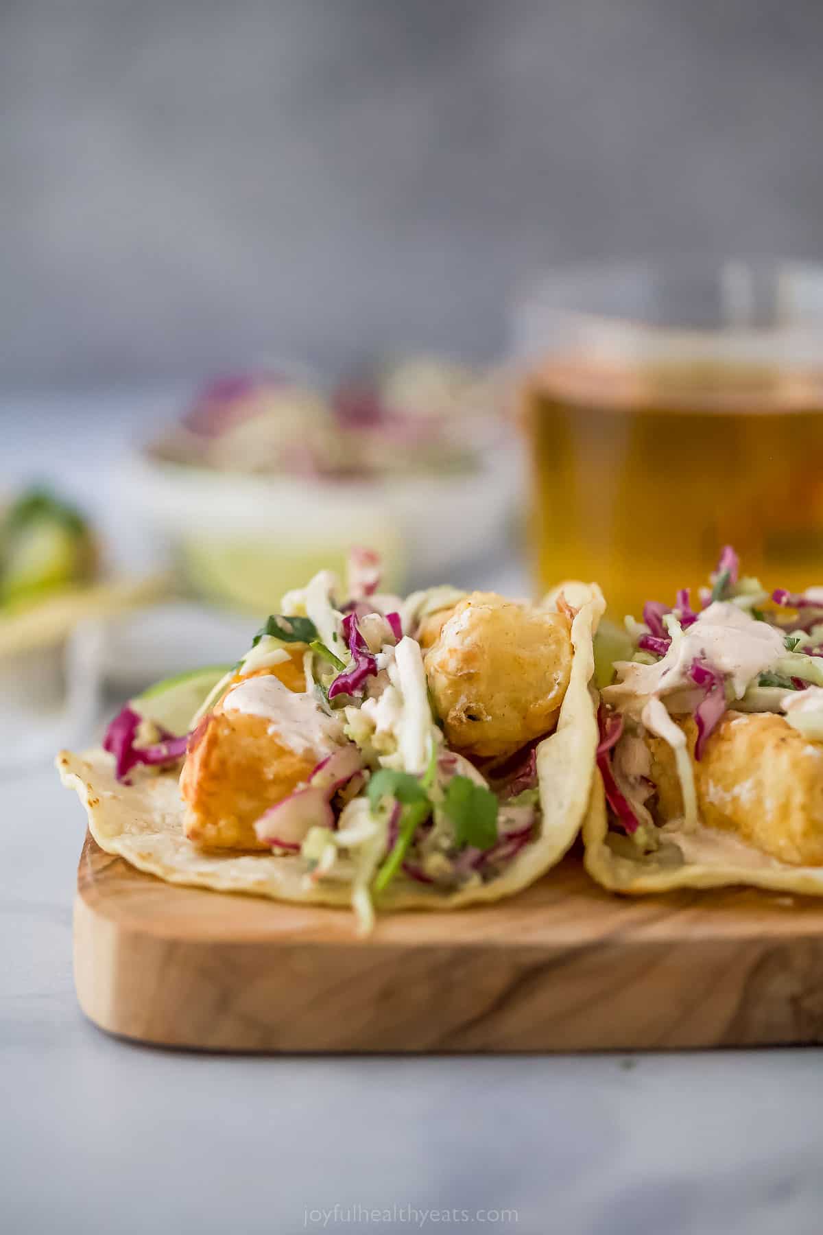 Beer Battered Air Fryer Fish Tacos are dipped in a tasty batter and fried the healthy way! Add slaw and Chipotle Crema for the perfect taco! side view of a taco with fried fish, coleslaw, and crema topping