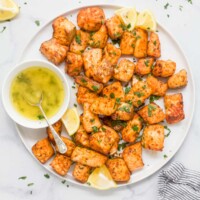 Air fryer salmon bites on a plate with lemon wedges and honey butter on the side.