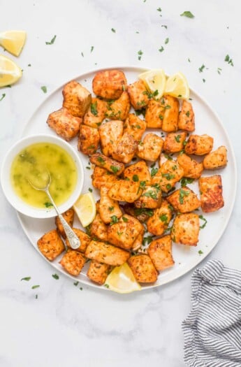 Air fryer salmon bites on a plate with lemon wedges and honey butter on the side.