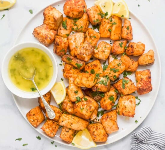 Air fryer salmon bites on a plate with lemon wedges and honey butter on the side.