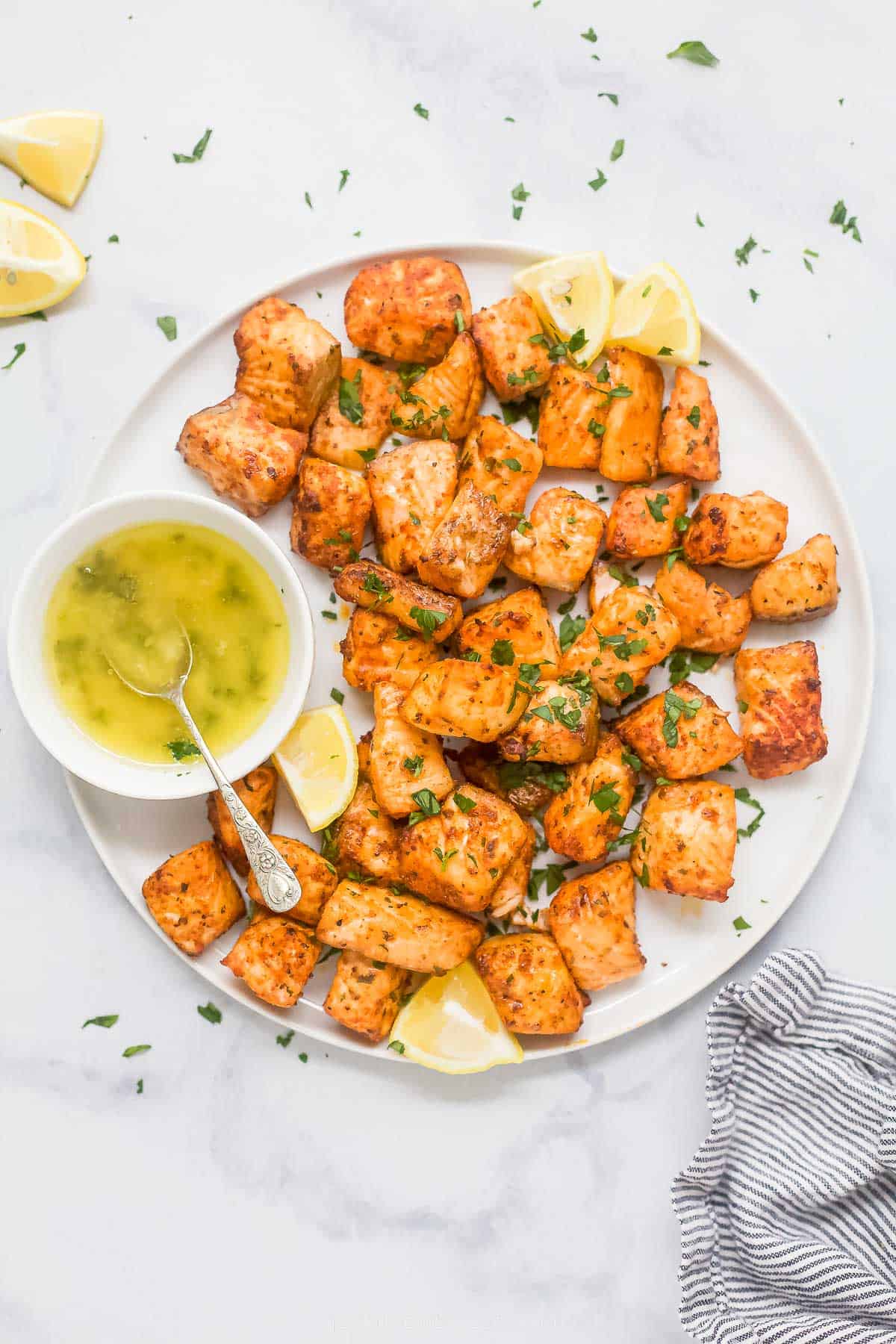 Air fryer salmon bites on a plate with lemon wedges and honey butter on the side. 