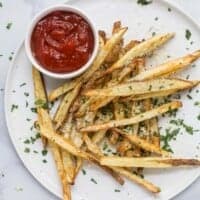Pommes frites on a plate with ketchup on the side.