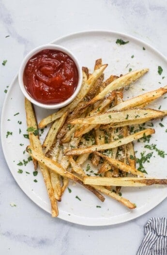 Pommes frites on a plate with ketchup on the side.