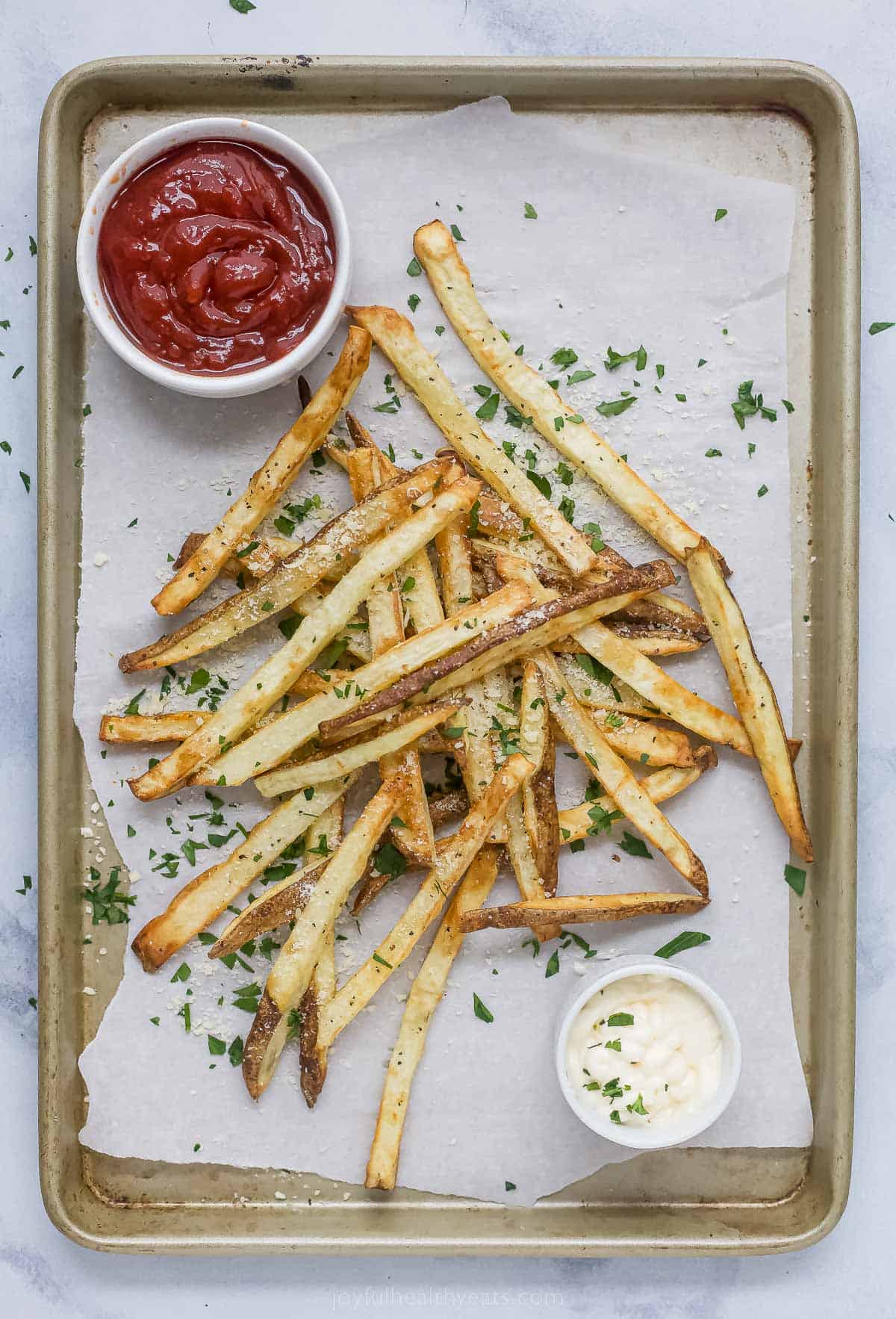 Pommes frites on a baking tray with dipping sauces on the side. 