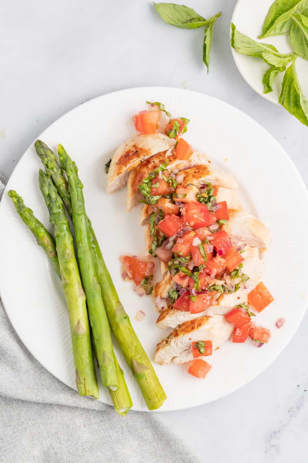 This juicy chicken bruschetta with an Italian-inspired summer veggie topping is the perfect 20-minute healthy but flavorful work lunch. Chicken bruschetta with a side of asparagus.
