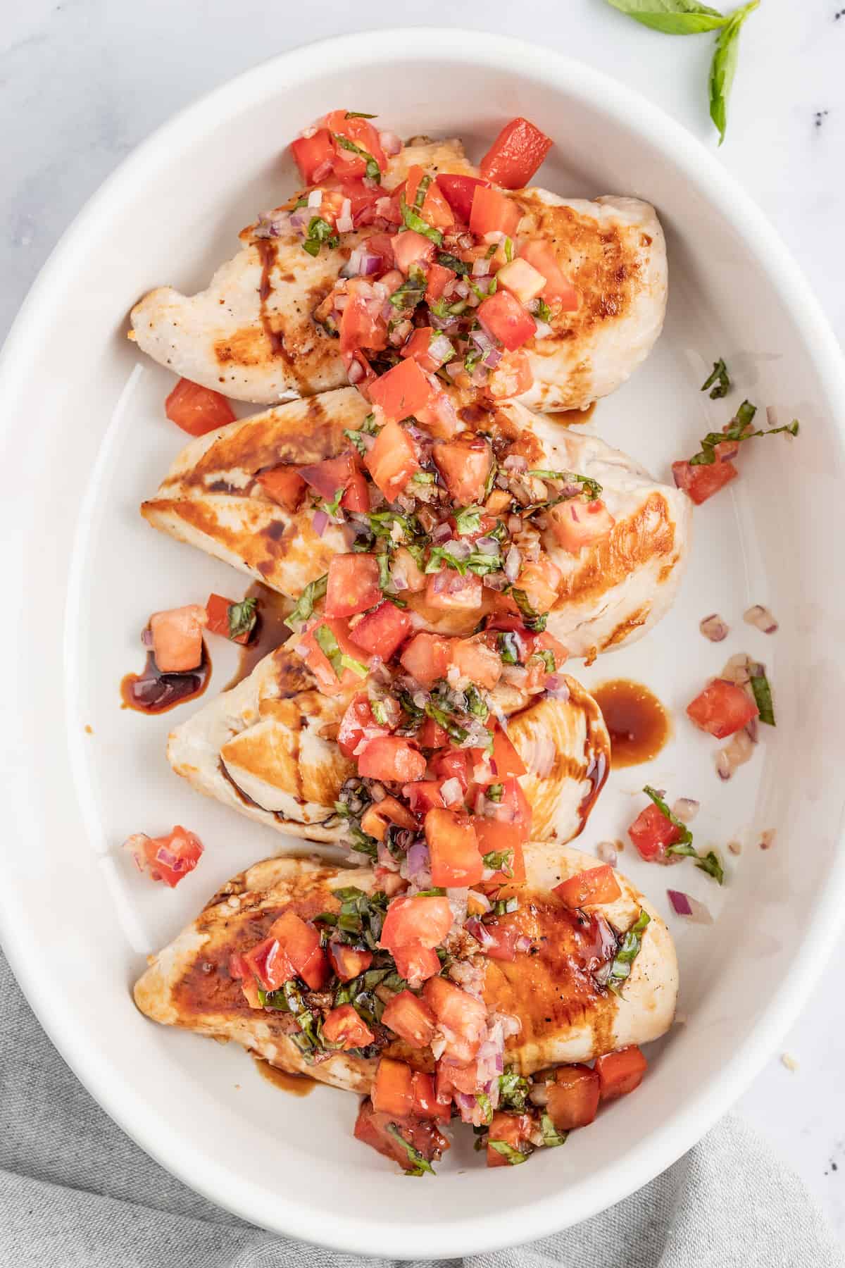 This juicy chicken bruschetta with an Italian-inspired summer veggie topping is the perfect 20-minute healthy but flavorful work lunch. Chicken bruschetta on a plate with balsamic reduction on top.