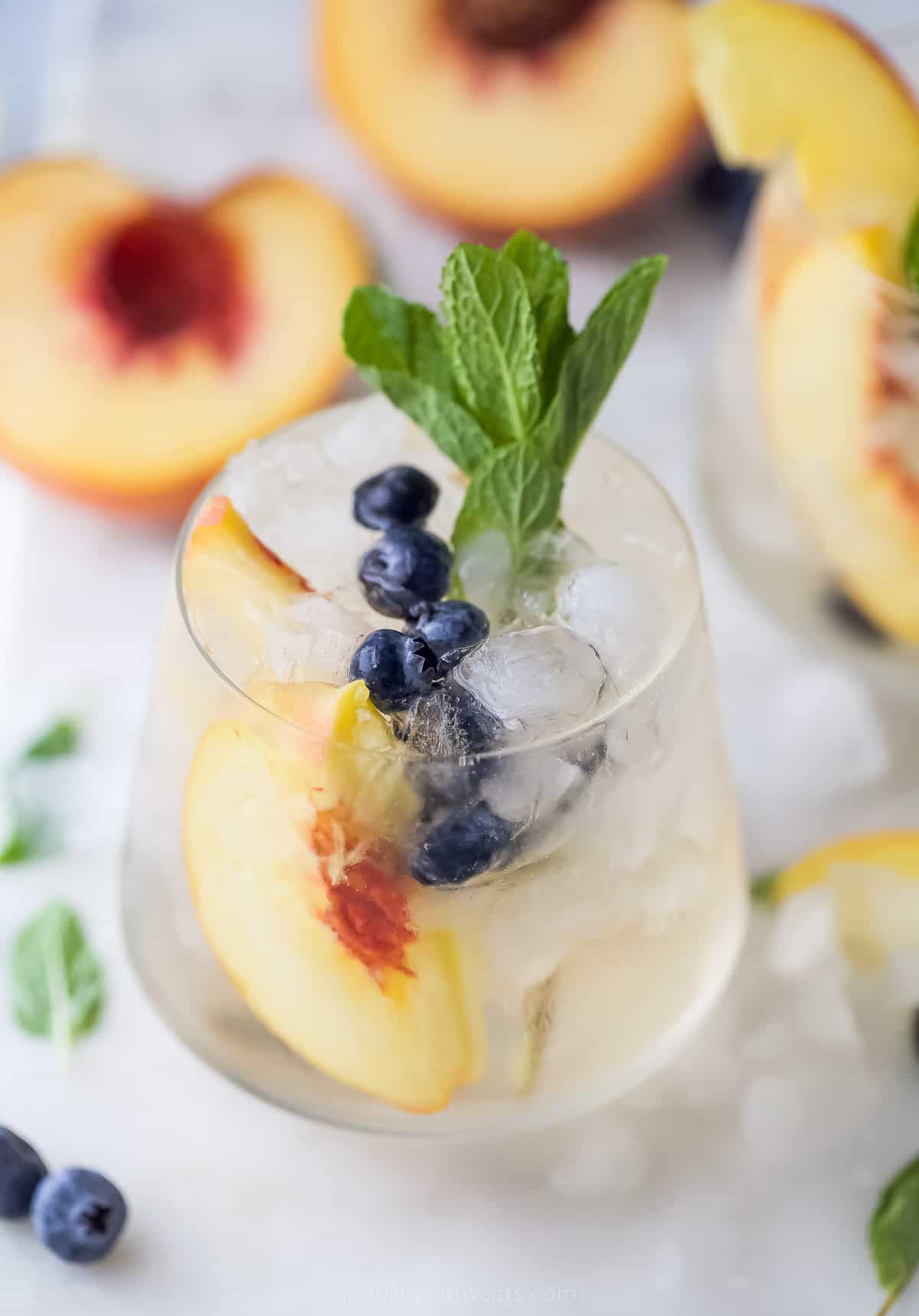 This icy peach sangria with blueberries, peach Schnapps, and mint is the fruity cocktail you'll be sipping on all summer. Close-up of peach sangria with fresh mint.