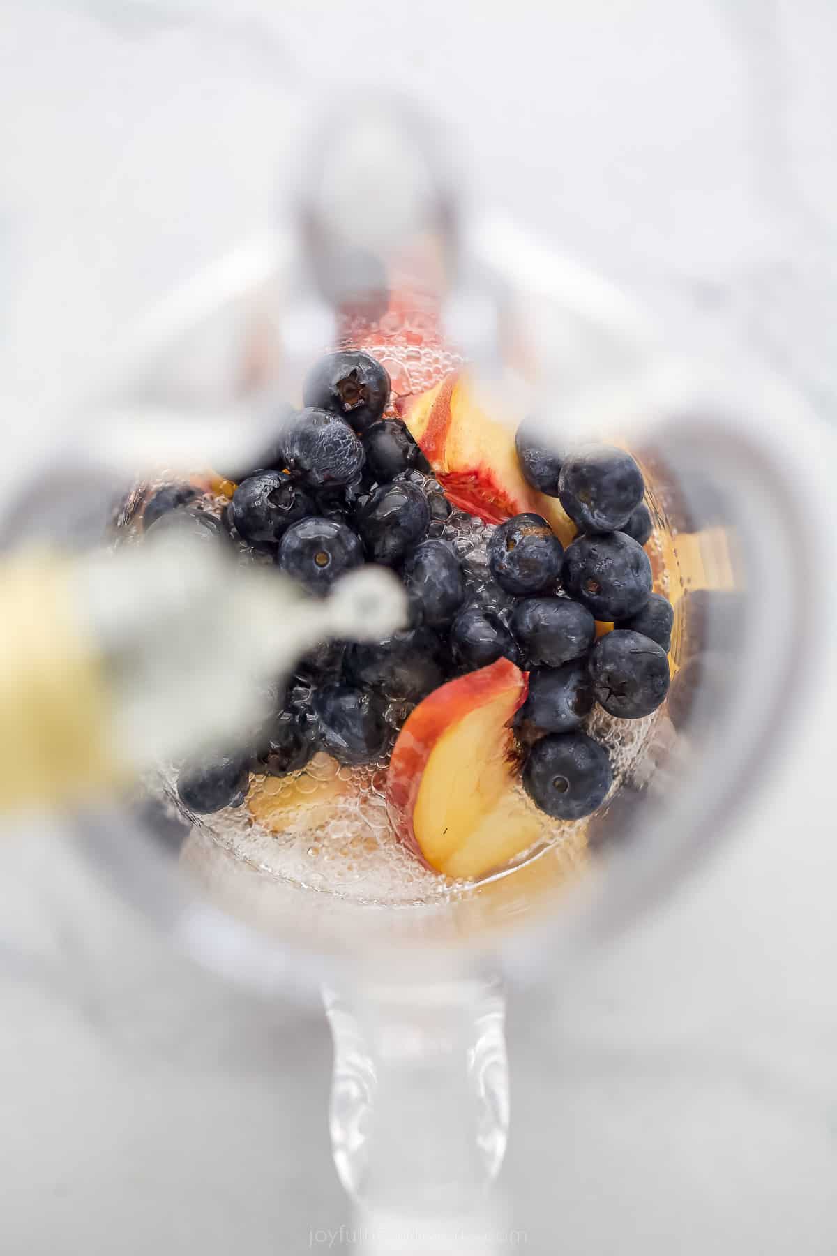 This icy peach sangria with blueberries, peach Schnapps, and mint is the fruity cocktail you'll be sipping on all summer. Pouring in the wine and Schnapps.