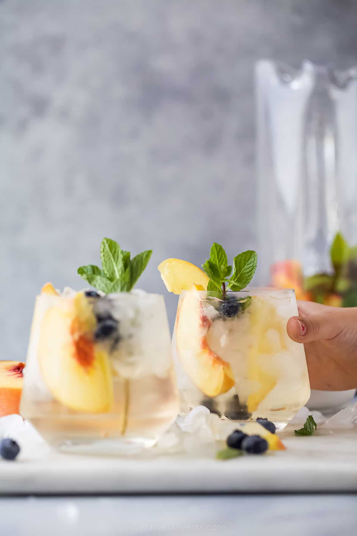 This icy peach sangria with blueberries, peach Schnapps, and mint is the fruity cocktail you'll be sipping on all summer. Grabbing a glass of peach sangria.