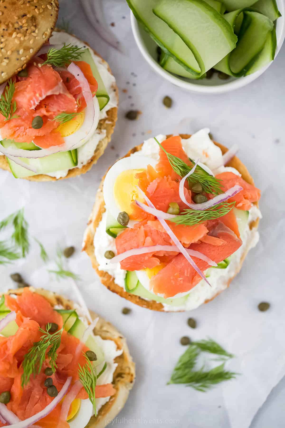 Three open bagels and lox with toppings and capers.