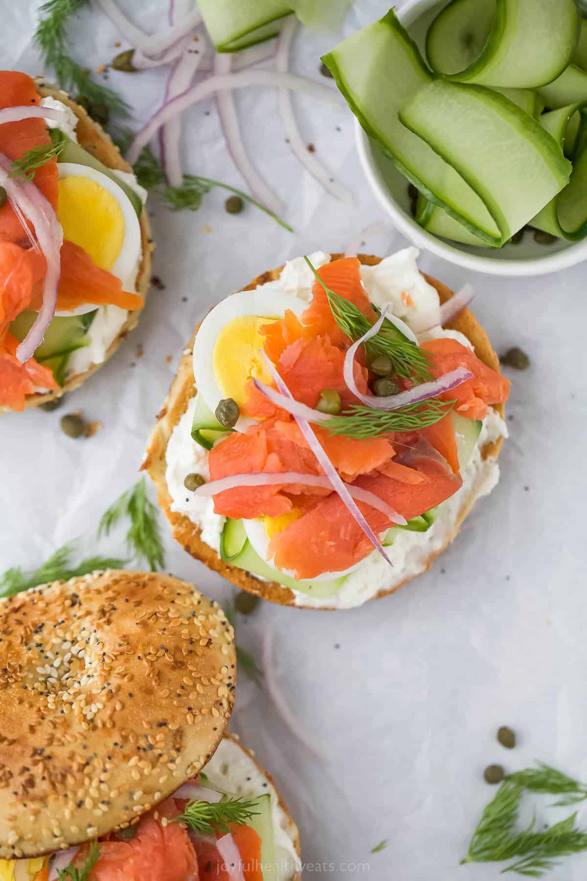 Topped with cream cheese, this bagel and lox recipe is the perfect 5-minute breakfast. It's crunchy, savory, spicy, and packed with veggies! Open bagel and lox with sliced cucumbers on the side.