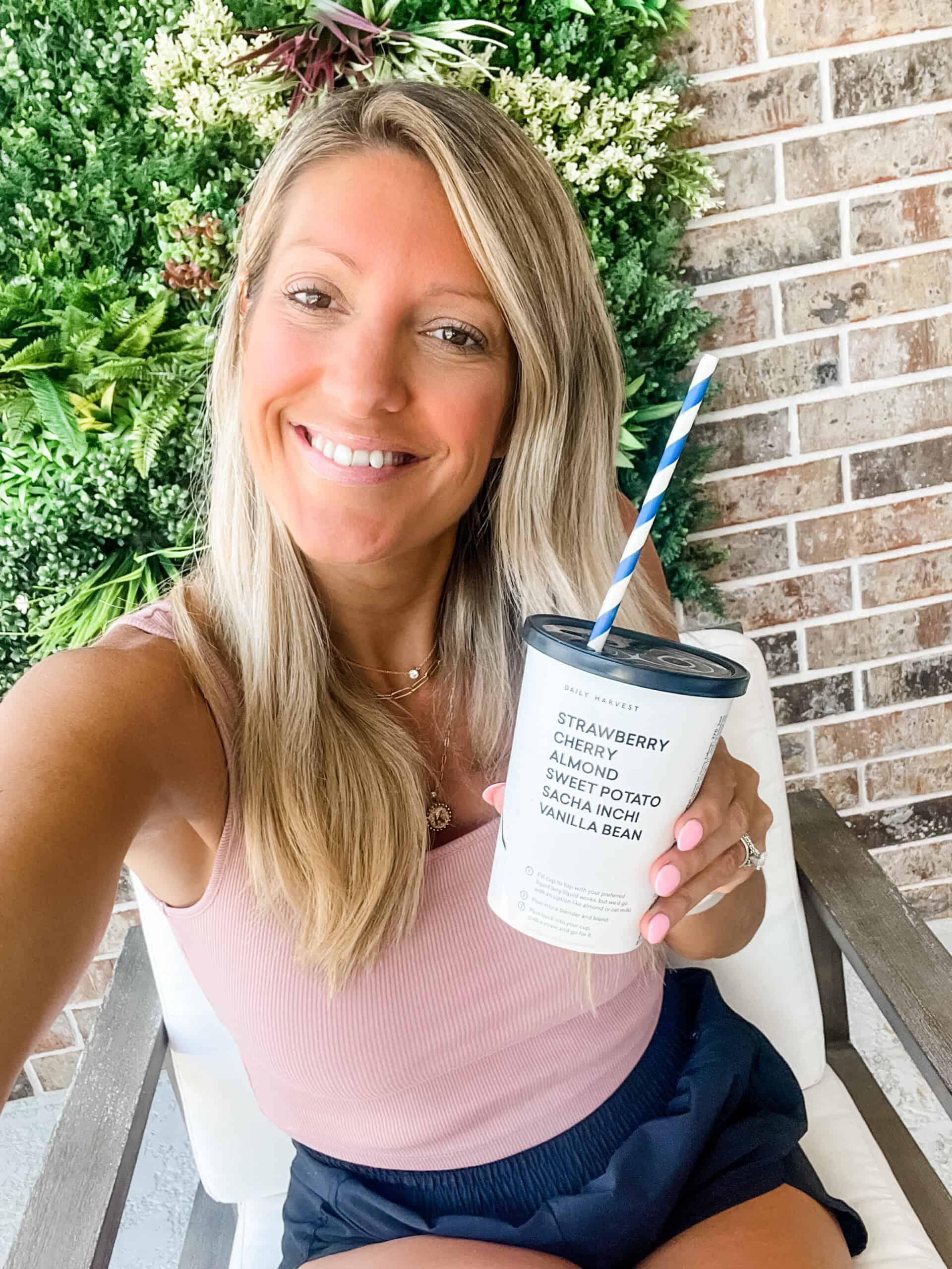 girl wearing workout girl holding a cherry + almond daily harvest smoothie