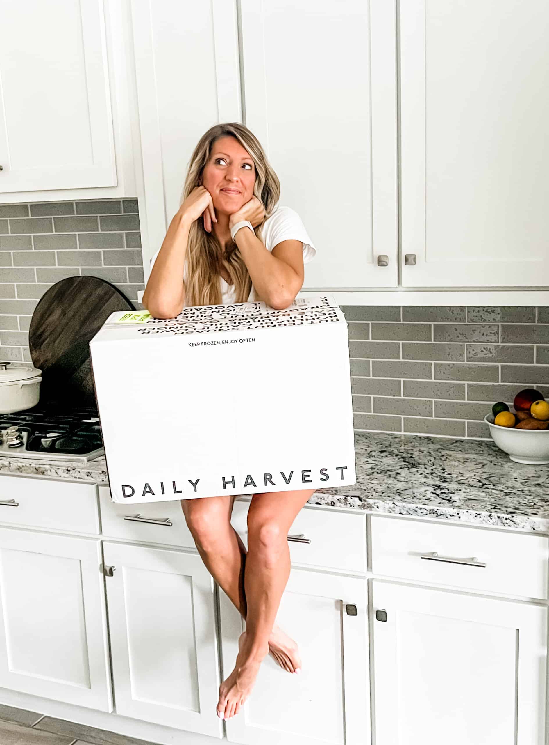 girls sitting on a counter with a box of daily harvest on her lap