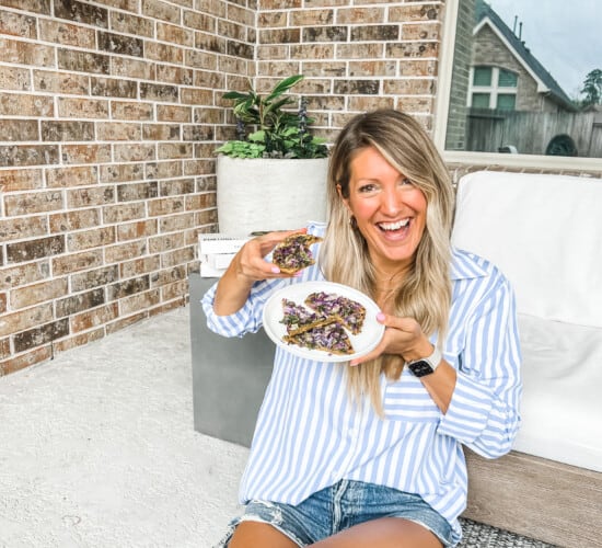 girl sitting on the floor holding daily harvest flatbread and smiling