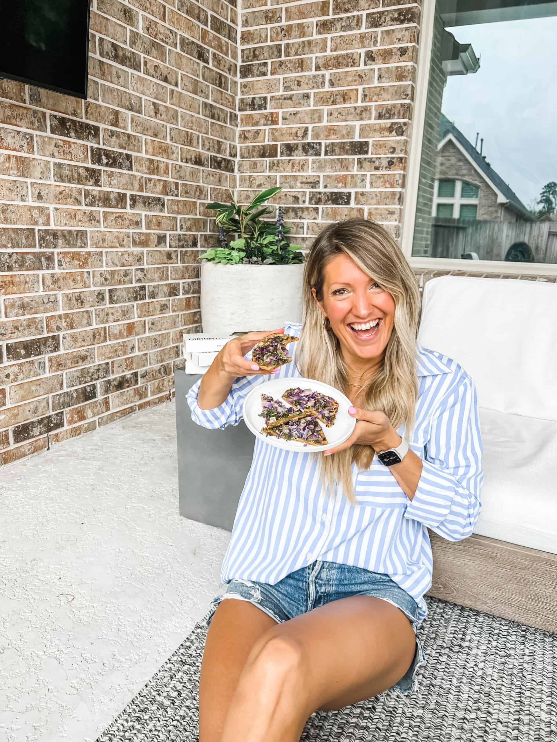 girl sitting on the floor holding daily harvest flatbread and smiling