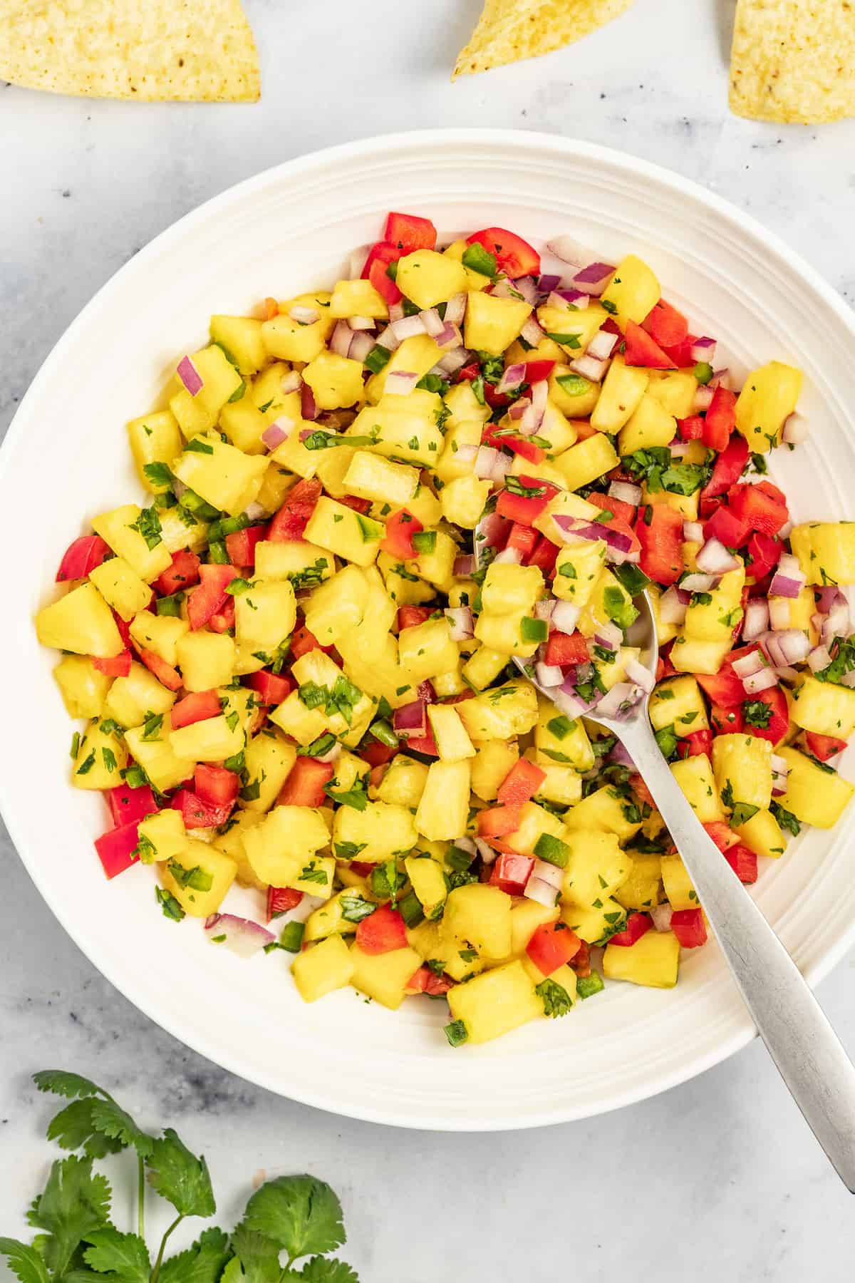 With bell pepper and jalapeño, this 15-minute pineapple salsa is a tangy, fruity, and crunchy addition to your all your meals. Bowl with pineapple salsa and a metal spoon.