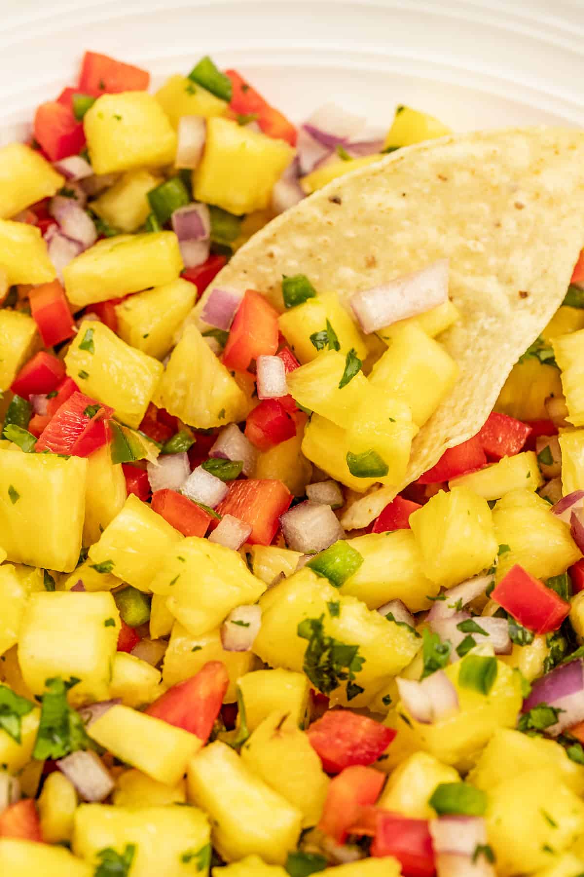 With bell pepper and jalapeño, this 15-minute pineapple salsa is a tangy, fruity, and crunchy addition to your all your meals. Dipping a corn chip into the pineapple salsa.