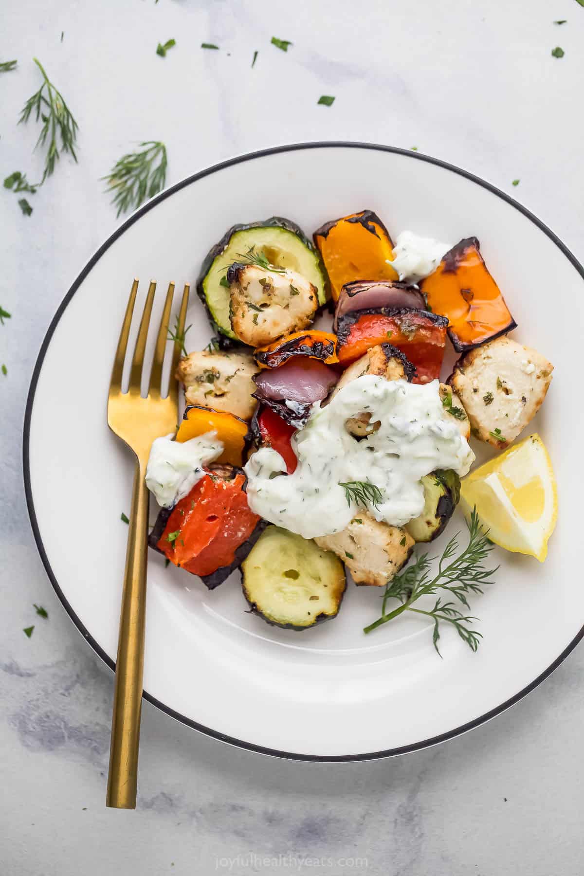 Reheated grilled chicken kabobs on a plate with tzatziki sauce.