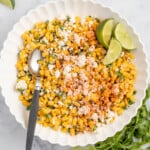 Mexican street corn in a bowl with lime wedges on the side.